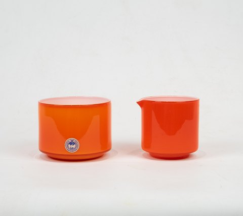 Orange glas sukkerskål og rød glas flødekande begge med hvidt opaline glas 
indvendigt fra Palet serien af Michael Bang for Holmegaard.
5000m2 udstilling.